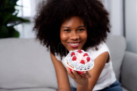 Photo for Beautiful young African blogger presenting cupcake with selective focus in concept special cuisine. Content creating of social media online with favorite sweets bakery dish. Tastemaker. - Royalty Free Image