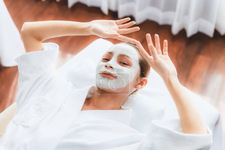 Photo for Serene daylight ambiance of spa salon, top view woman lying on massage table smiling and rejuvenating with face cream spa massage. Facial skin spa treatment and beauty care concept. Quiescent - Royalty Free Image