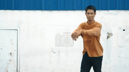 Photo for Hispanic man stretch arms and dance break dancing in front of wall. Motion shot of stylish street dancer in casual outfit practicing dancing in hip hop style. Outdoor sport 2023. Background. Endeavor. - Royalty Free Image