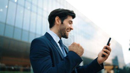 Photo for Successful business man celebrate increasing sales while standing. Happy project manager or leader proud with successful project, getting a promotion, getting a job while holding a phone. Exultant. - Royalty Free Image