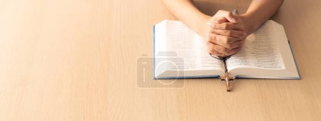 Photo for Cropped image of praying male hand holding cross on holy bible book at wooden table. Top view. Concept of hope, religion, faith, christianity and god blessing. Warm and brown background Burgeoning. - Royalty Free Image