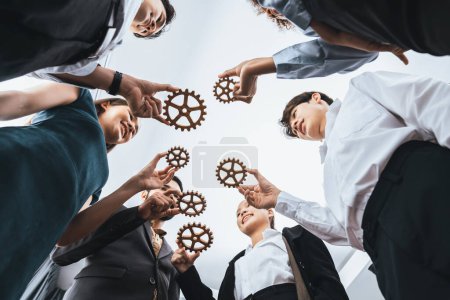 Photo for Below view office worker holding cog wheel as unity and teamwork in corporate workplace concept. Diverse colleague business people as symbol of visionary system teamwork for business success. Concord - Royalty Free Image