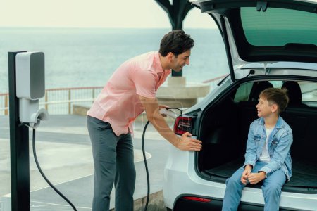 Photo for Family road trip vacation traveling by the sea with electric car, father and son recharge EV car with green and clean energy. Natural travel and eco-friendly car for sustainable environment. Perpetual - Royalty Free Image