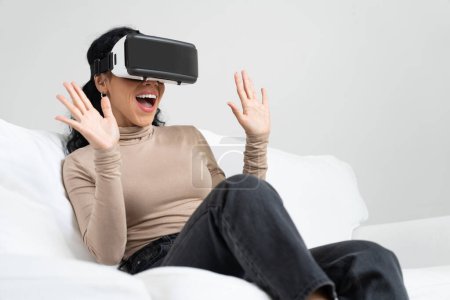 Foto de Mujer joven que usa gafas VR de realidad virtual en casa para una experiencia de compra en línea crucial. La innovación de realidad virtual VR optimizada para el estilo de vida de entretenimiento digital femenino. - Imagen libre de derechos