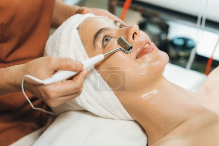 Photo for Beautiful caucasian woman lying on spa bed during having facial massage by professional hands at modern spa salon surrounded by beauty electrical equipment or medical equipment. Close up. Tranquility - Royalty Free Image