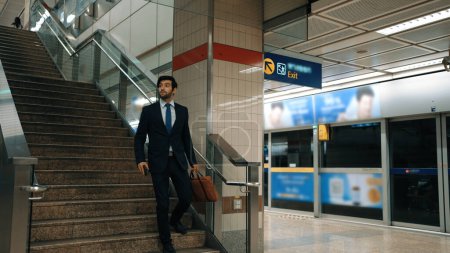 Téléchargez les photos : Homme d'affaires caucasien professionnel descendant l'escalier pour le métro ou le train du ciel tout en allant au travail. Responsable de projet qualifié utilisant les transports publics tout en portant une combinaison formelle. Heure de pointe. Exultant. - en image libre de droit