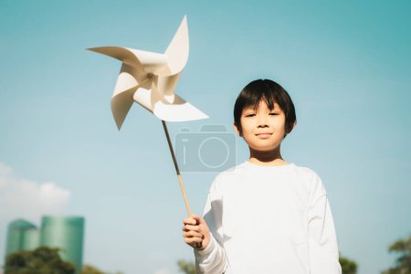 Foto de Pequeño niño asiático sosteniendo molino de viento o modelo de maqueta de turbina eólica para promover la utilización de tecnología de energía limpia y renovable ecológica para la generación futura y la Tierra sostenible. Gyre. - Imagen libre de derechos