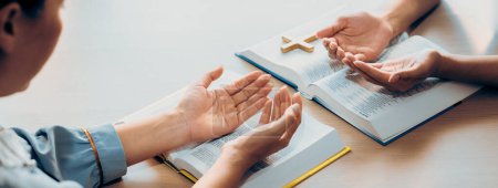 Photo for Two believer praying together on holy bible book faithfully with wooden cross placed at wooden church. Concept of hope, religion, faith, christianity and god blessing. Facing hand. Burgeoning. - Royalty Free Image