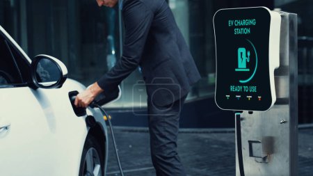 Photo for Businessman recharge his electric car from charging station at city center or public car park. Eco friendly rechargeable car using alternative clean energy in urban city lifestyle.Peruse - Royalty Free Image