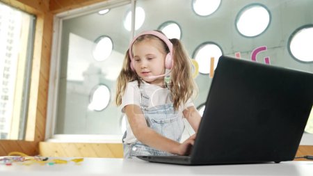 Photo for Smart caucasian girl wearing headphone and looking at electronic equipment. Skilled student working by using laptop to searching and learning electric equipment on table. Smart classroom. Erudition. - Royalty Free Image