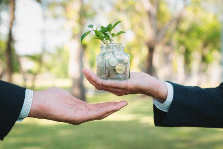 Konzept der nachhaltigen Geldanlage mit Glasgefäß gefüllt mit Sparmünzen bei Geschäftsleuten als umweltfreundliche Geldanlage, die mit der Natur und einem gesunden Ruhestand gepflegt wird. Kreisel