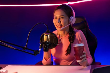 Photo for Host channel of creative broadcast listening the music on social media with listeners holding coffee up, wearing pastel color headphones, using mic radio record by camera at neon studio. Stratagem. - Royalty Free Image