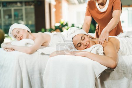 Un retrato de dos mujeres jóvenes y atractivas yacen en la cama durante el masaje de espalda por un masajista profesional al aire libre rodeado de un entorno natural tranquilo. Concepto saludable y de belleza. Tranquilidad.