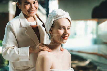Téléchargez les photos : Attractives femmes caucasiennes reçoit massage du dos avec sourire visage par masseur professionnel thaïlandais tout en étant assis entouré par un environnement spa paisible. Santé et beauté. Fond flou. Tranquillité. - en image libre de droit
