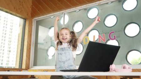 Photo for Happy girl looking at camera while raised hands to celebrate success project. Smart cute student finish writing, programing system and shouting with happiness in STEM technology class work. Erudition. - Royalty Free Image