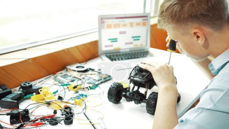 Photo for Top view of happy student study car model construction at table with electronic equipment and laptop display coding program screen scatter around at STEM classroom. Creative education. Edification. - Royalty Free Image