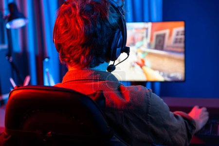 Photo for Host channel of young gaming streamer, team gamer playing battle game shooting with multiplayer at warship on pc screen with back side image, wearing headset with mic at digital neon room. Gusher. - Royalty Free Image