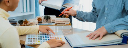 Photo for Cropped image of professional interior design team discuss about color and material usage for the project while project manager choose main theme color with house model on meeting table. Variegated. - Royalty Free Image