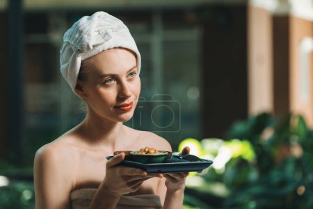 Photo for Portrait of beautiful caucasian woman in white towel holds the tray which contained the bowl of herbal scrub and spa rock surrounded by calm and relaxing nature. Side view. Tranquility. - Royalty Free Image