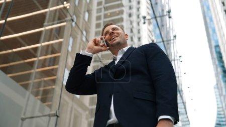Téléchargez les photos : Vue de la caméra basse angle de l'homme d'affaires appelant au gestionnaire tout en discutant du plan d'affaires avec vue sur gratte-ciel. Responsable de projet professionnel travaillant sur le téléphone et partageant des idées marketing. Urbane. - en image libre de droit