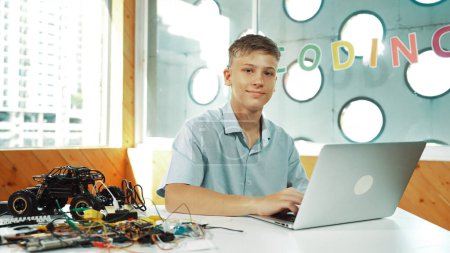 Teenager, die am Laptop arbeiten und im MINT-Technikunterricht in die Kamera schauen. Kaukasische High-School-Schüler mit Computer, um Daten zu analysieren, während sie auf die Kamera auf dem Tisch mit Auto-Modell schauen. Erbauung.