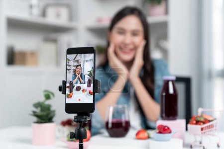 Photo for Selective focus smartphone with smiling young beautiful Asian reviewing mixed strawberry and cherry juice detox drink, presenting healthy product promotion selling on social media online. Stratagem. - Royalty Free Image