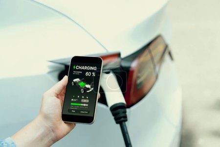 Photo for Hand insert EV charger plug into electric vehicle to recharge EV car, battery status display on smartphone EV application. Future alternative clean and sustainable energy for transportation. Perpetual - Royalty Free Image