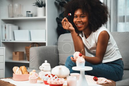 Téléchargez les photos : Belle jeune blogueuse africaine présentant un morceau de cupcake en concept montrant une cuisine spéciale en couleur pastel. Création de contenu de médias sociaux avec plat préféré de boulangerie de bonbons. Tastemaker. - en image libre de droit