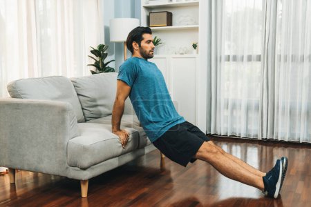 Athletischer Körper und aktiver, sportlicher Mann mit Möbeln zur effektiven gezielten Muskelaufbauübung bei fröhlicher Heimübung als Konzept eines gesunden, fitten Körpertrainingsstils.