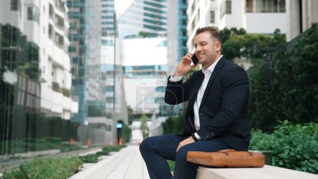 Photo for Caucasian businessman sitting at bench while talking to manager by using phone about planning strategy. Professional executive manager calling marketing team and sharing creative idea at city.Urbane. - Royalty Free Image
