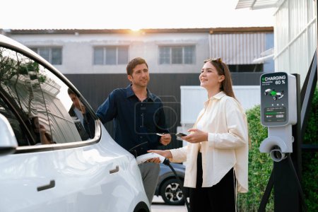 Photo for Eco-friendly conscious family couple recharging EV vehicle from home charging station. EV electric car technology utilized as alternative transportation for future sustainability. Expedient - Royalty Free Image