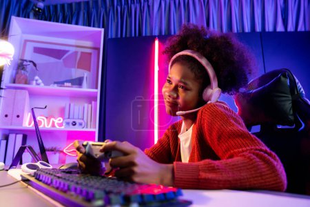 Photo for African American girl streamer playing online fighting with Esport skilled team wearing headphones in neon color lighting room. Talking other players planing strategies to win competitors. Tastemaker. - Royalty Free Image