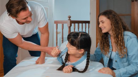 Glückliche moderne Familien wecken ihr kleines Mädchen am Wochenende mit spielerischem Kitzeln, indem sie ihre Liebe und Zuneigung zu ihrer kleinen Tochter zum Ausdruck bringen, gemeinsam lachen und lächeln. Panorama-Synchronen