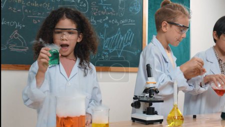 Photo for Children doing experiment in science lesson while standing at blackboard at laboratory. Happy student discovering and learning about biochemical liquid while inspecting and mixing sample. Pedagogy. - Royalty Free Image