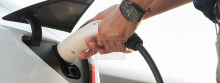 Photo for Closeup hand put EV charger to recharge electric cars battery in city commercial parking lot. Rechargeable EV car for sustainable environmental friendly urban travel. Panorama Expedient - Royalty Free Image