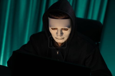 Foto de Máscara blanca criminal anónimo instalación de cifrado de contraseña mediante la programación hackear, tratando de hacer que la privacidad a fondo inseguro tomar base de datos masiva en la computadora para el rescate a la empresa. Pecuniario. - Imagen libre de derechos