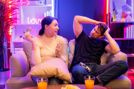 Photo for Smiling beautiful woman winner fighting gamer on video game beside loser man. Couple joyful of player on TV using joysticks in studio room in red blue neon light at Comfy living home place. Postulate. - Royalty Free Image