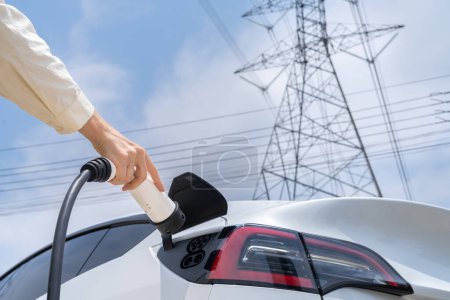 Photo for Closeup woman recharge EV electric car battery at charging station connected to electrical power grid tower on sky background as electrical industry for eco friendly vehicle utilization. Expedient - Royalty Free Image