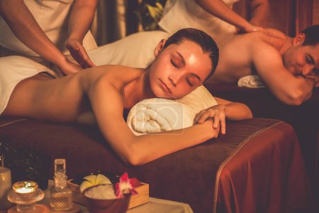 Photo for Caucasian couple customer enjoying relaxing anti-stress spa massage and pampering with beauty skin recreation leisure in warm candle lighting ambient salon spa at luxury resort or hotel. Quiescent - Royalty Free Image