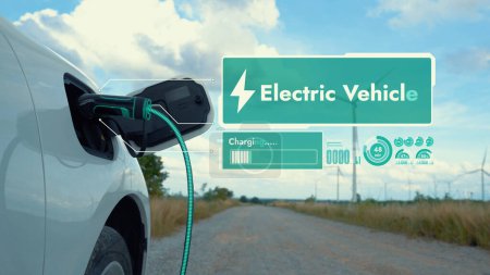 Photo for Electric car recharging energy from EV charging station display futuristic smart battery status hologram by EV charger plug cable in wind turbine farm. Alternative clean energy sustainability. Peruse - Royalty Free Image