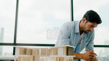 Photo for Smart caucasian engineer or project manager measure check, inspect, look at house model while standing near panorama window with city, skyscraper view. Manager design house construction. Tracery - Royalty Free Image