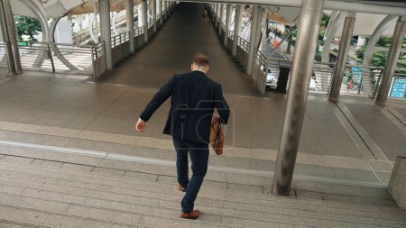 Photo for Businessman walking down stair and hurry to walking back to home. Back view of business people wearing suit and celebrate for getting promotion or increasing sales while holding his suitcase. Urbane. - Royalty Free Image
