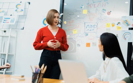 Leader attrayant professionnel féminin présente un plan de marketing créatif en utilisant un graphique statistique de brainstorming mind mapping et une note collante colorée dans la salle de réunion d'affaires moderne. Immaculée.