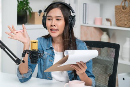 Photo for Host channel Asian influencer talking in broadcast streaming online wearing headset on social media live with script note, greeting listeners in life coaching or marketing at modern studio. Stratagem. - Royalty Free Image