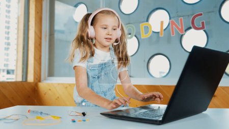 Photo for Young student working on laptop or studying in online classroom. Caucasian girl typing on laptop while doing homework or listening music.Little kid wearing headphone. Creative learning. Erudition. - Royalty Free Image