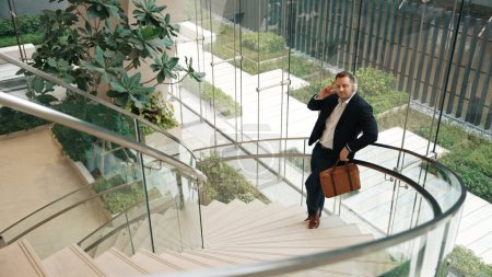Vue de dessus de l'homme d'affaires caucasien écoutant de la musique relaxante portant un casque tout en se tenant debout à des escaliers en colimaçon dans un bâtiment moderne. Le chef de projet aime écouter la chanson tout en passant à la rime. Urbane.