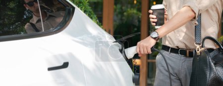 Photo for Eco friendly man and sustainable urban commute with EV electric car recharging at outdoor cafe in springtime garden, green city sustainability and environmental friendly EV car. Panorama Expedient - Royalty Free Image