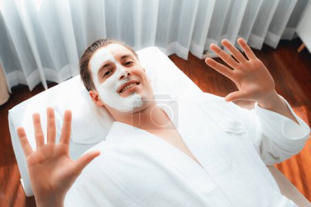 Téléchargez les photos : Ambiance sereine de salon de spa, client homme se livre à rajeunir avec massage crème visage luxueux avec la lumière du jour moderne. Soin du visage et concept de soins de beauté. Tranquillité - en image libre de droit