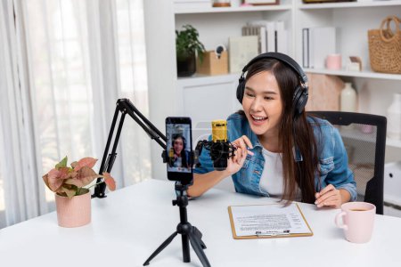 Photo for Host channel Asian influencer talking in broadcast wearing headsets on social media live on smartphone recording online, greeting listeners with coaching life or business at modern studio. Stratagem. - Royalty Free Image