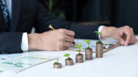Businessman with coin stack at his office as sustainable money growth investment or eco-subsidize. Green corporate promot and invest in environmental awareness. Gyre